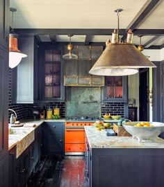 an instagramted photo of a kitchen with orange cabinets and black appliances, including a large pendant light over the island