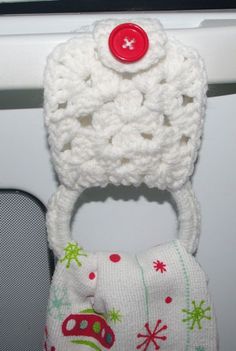 a white knitted hat with a red button on the top is hanging from a hook