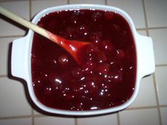 a white bowl filled with cherries on top of a tiled floor next to a wooden spoon