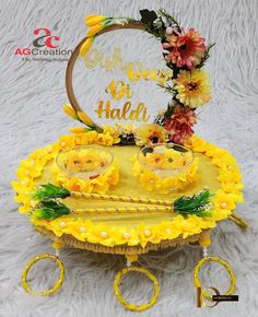 a cake with yellow flowers on it sitting on top of a white table next to two gold rings