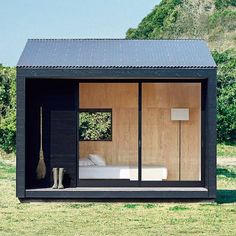 a small black cabin with sliding glass doors and a bed in the corner on grass