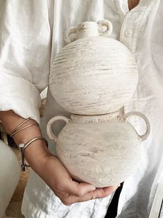 a person holding two white vases in their hands