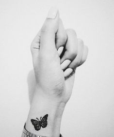 a black and white photo of a woman's wrist with a butterfly tattoo on it