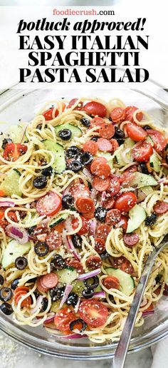 pasta with tomatoes, olives and other vegetables in a glass bowl next to a fork