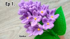 a crocheted purple flower sitting on top of a green leaf