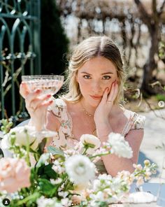 a woman sitting at a table with a glass of wine in front of her face