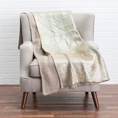 a chair with a blanket on it in front of a white brick wall and wooden floor