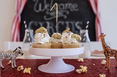 cupcakes with white frosting and zebra figurines on a cake stand