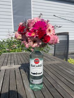 a bottle of bacardi water sitting on a wooden table with flowers in it