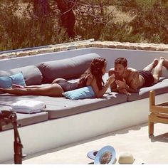 a man and woman laying on top of a couch next to each other near a pool