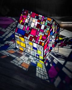 a colorful cube sitting on top of a wooden floor next to a shadow cast wall