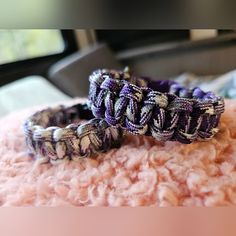 two purple and white bracelets sitting on top of a pile of pink fluffy material