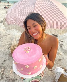 a woman holding a pink cake on the beach