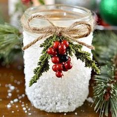 a glass jar filled with white snow and red berries sitting on top of a wooden table