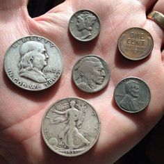 a person's hand holding five different types of coins