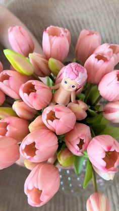 a vase filled with pink tulips on top of a white tablecloth next to a small doll