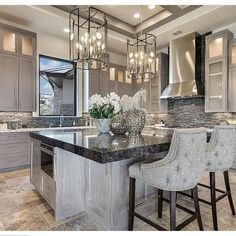 a large kitchen with marble counter tops and gray cabinets, along with two bar stools