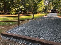 a truck is parked on the side of a gravel road near a fence and trees