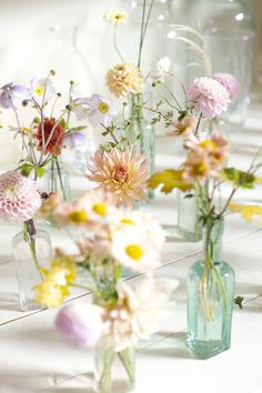 several vases filled with different types of flowers on a white tableclothed surface