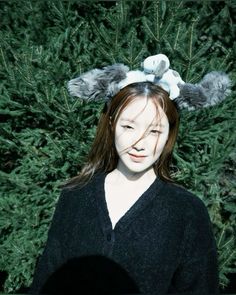 a woman with long hair wearing a black sweater and grey bunny ears on her head