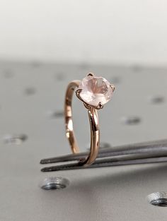 a pink diamond ring sitting on top of a piece of metal next to some nails