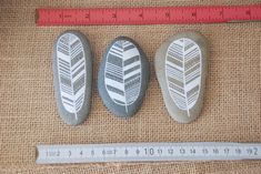 three rocks with designs on them next to a ruler