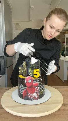 a woman in black shirt and white gloves decorating a cake with spiderman decorations