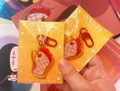 someone is holding up two plastic keychains that are shaped like heart - shaped bags