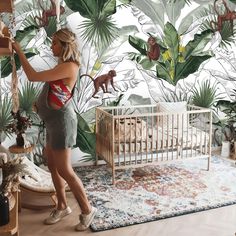 a woman standing next to a baby crib in front of a jungle wallpaper