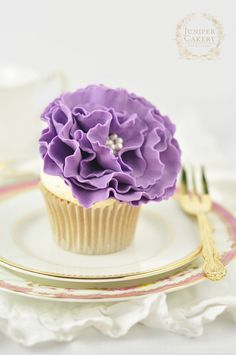 a cupcake with purple icing on a plate next to a fork and knife