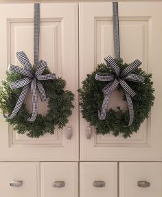 two wreaths hanging on the front door of a white cabinet with black and white bows