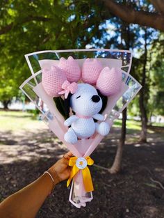 a hand holding a stuffed animal with pink bows on it's head and ribbon around its neck