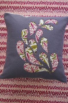 a blue pillow with pink and green flowers on it, sitting on a quilted surface