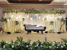 a couch sitting on top of a stage covered in flowers and greenery next to a clock