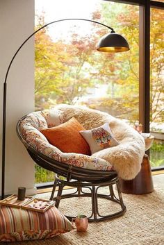 a living room with a chair, floor lamp and large window overlooking the trees outside