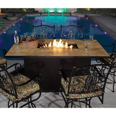 an outdoor table with chairs around it and a fire pit in the middle, next to a swimming pool