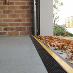 a window sill with leaves on the ground next to it and a brick wall in the background