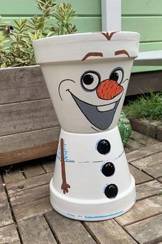 a snowman pot sitting on top of a wooden deck next to a planter