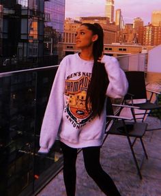 a woman standing on top of a roof with her hair in a ponytail wearing a sweatshirt and leggings