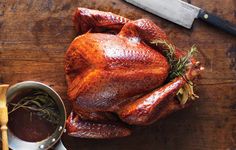 a roasted turkey on a wooden table next to a pot of gravy and a knife