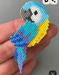 a hand holding a small beaded brooch with a blue bird on it's back