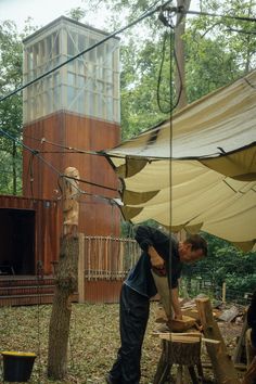 a man is working on a piece of wood in the woods next to a building