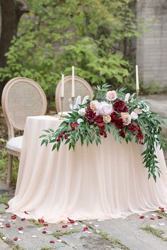 a table with flowers and candles on it in the middle of a stone path surrounded by greenery