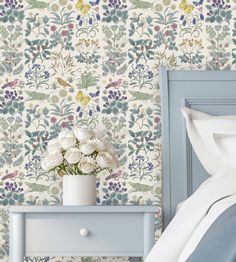 a blue nightstand with flowers on it next to a wallpapered bed and night stand