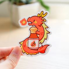 a hand holding up a sticker with an image of a red dragon on it