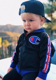 a little boy sitting on top of a white car wearing a black jacket and hat