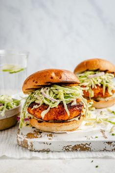 two chicken burgers with coleslaw slaw on top and another sandwich in the background