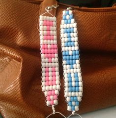 two beaded earrings sitting on top of a brown leather bag next to a purse