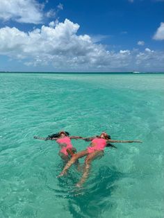 two women in pink swimsuits floating in the ocean with their arms around each other