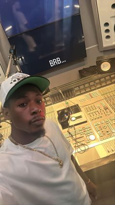 a man wearing a green hat sitting in front of a mixing desk with electronic equipment